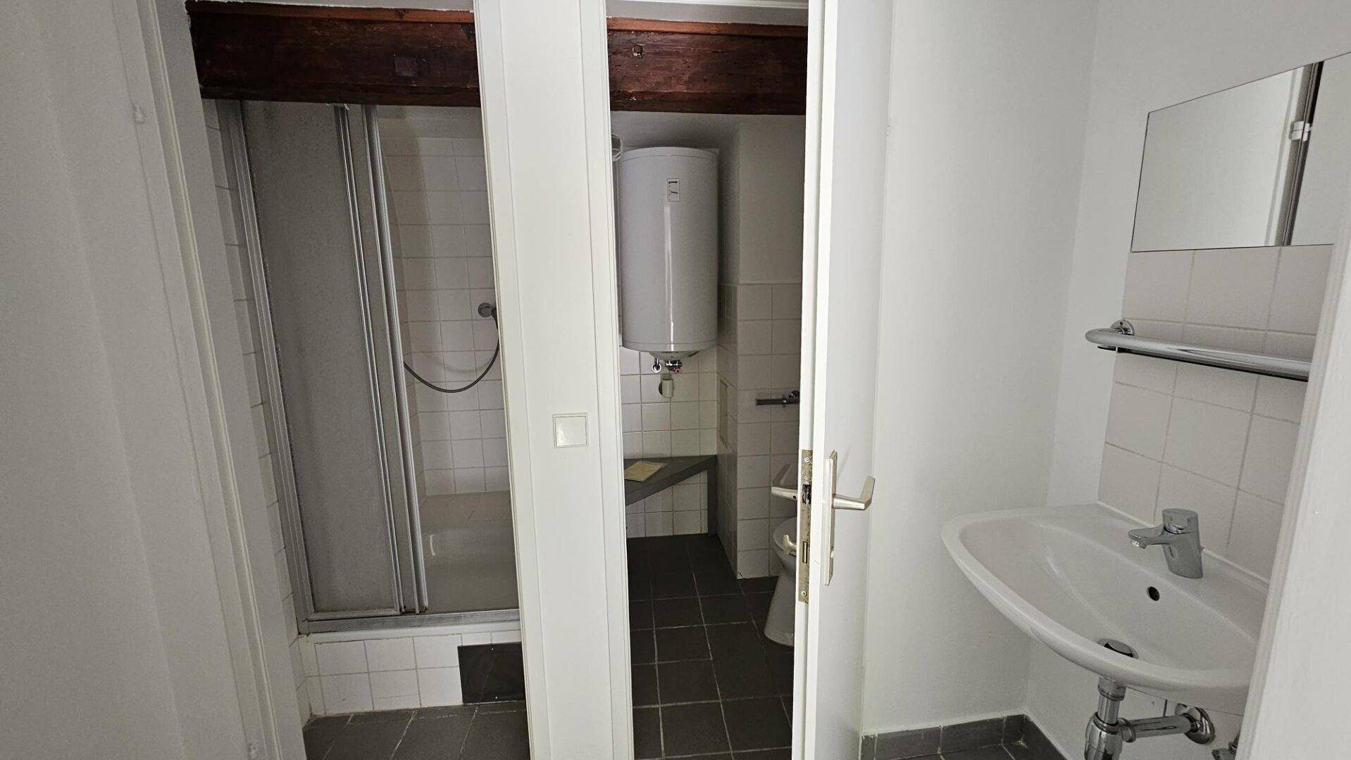 Kompaktes Badezimmer mit Dusche, Waschbecken, Toilette und Warmwasserboiler, funktional eingerichtet.