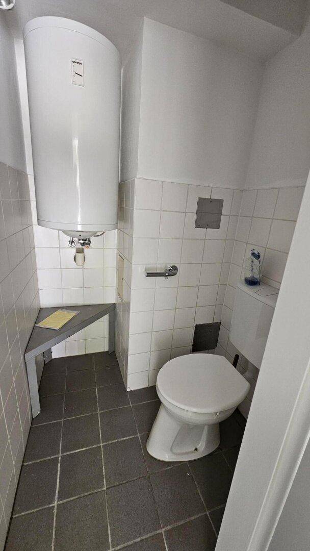 Toilettenbereich mit wandmontiertem Warmwasserboiler und weißen Wandfliesen, praktisch und platzsparend.