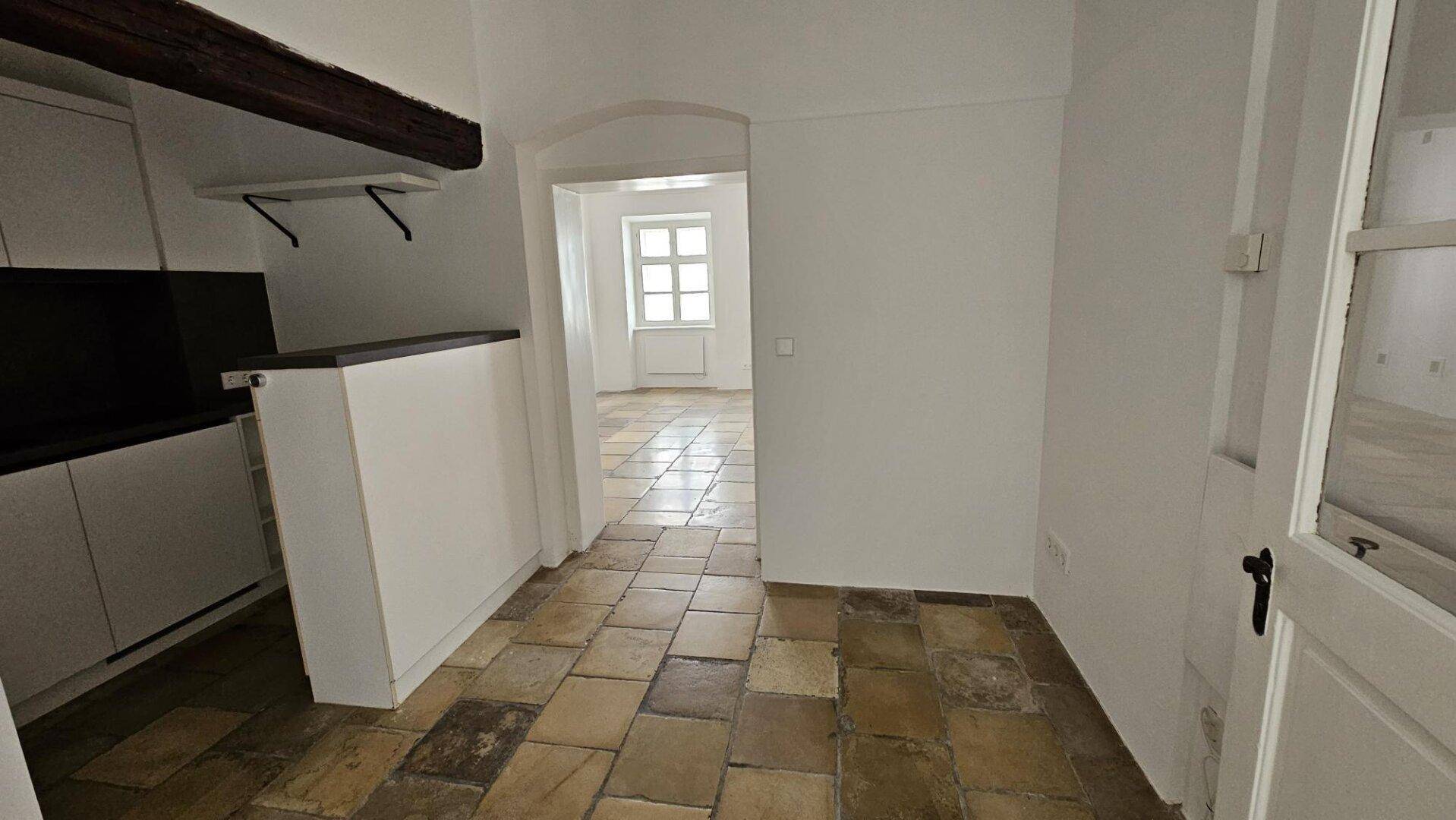 Blick vom Küchenbereich durch einen Rundbogen in einen angrenzenden Raum mit gleichem Steinboden.