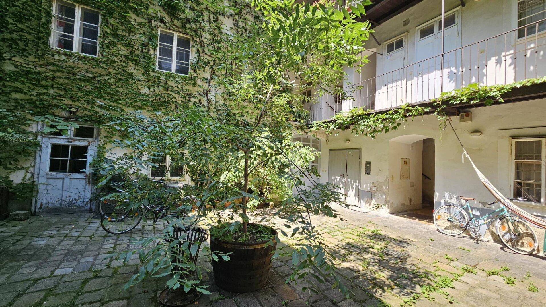 Malerischer Innenhof mit zentralem Baum, Kopfsteinpflaster und begrünten Fassaden, ideal zum Entspannen.