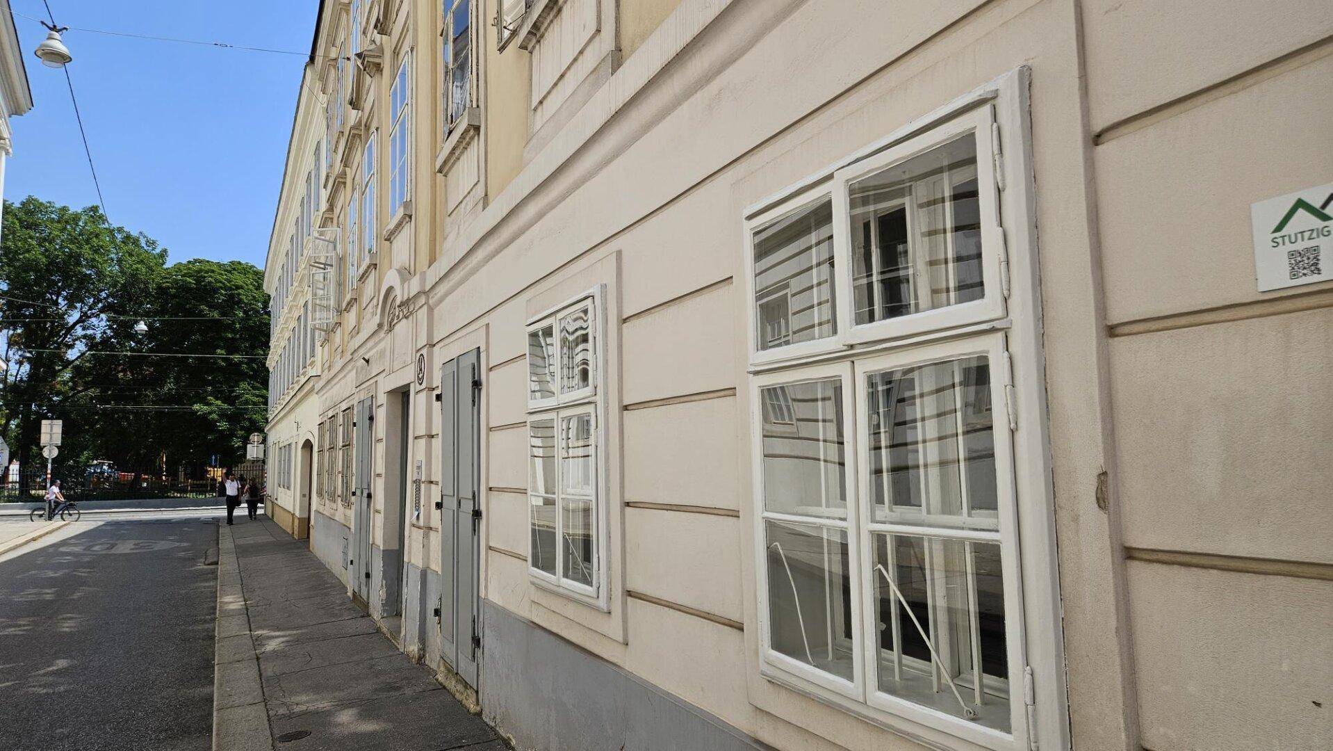 Historische Fassade eines Gebäudes an einer ruhigen Straße mit vielen Fenstern und klassischer Architektur.