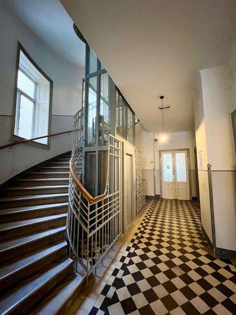 Helles Treppenhaus mit historischem Fliesenboden, hohen Decken und modernem Aufzug.