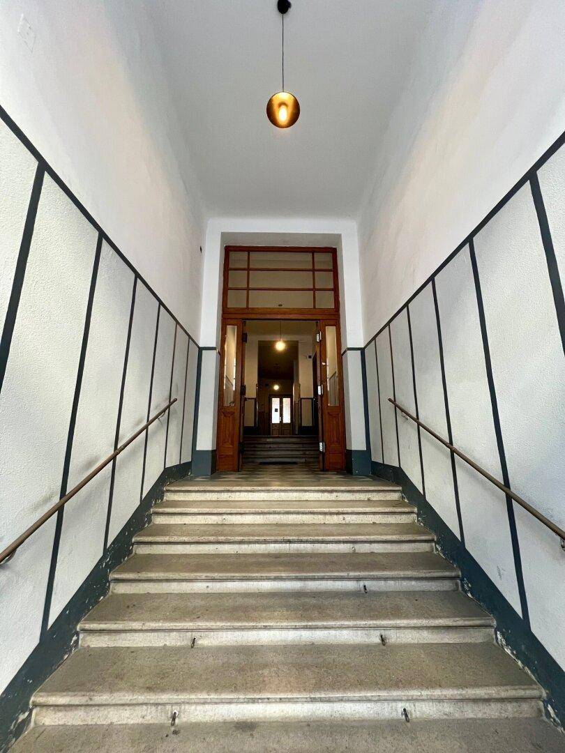 Eingangsbereich mit breiter Steintreppe und hohen Decken in einem gepflegten Altbau.