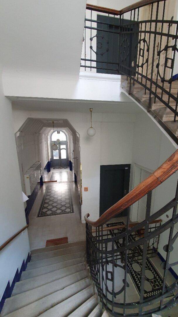 Historisches Treppenhaus mit kunstvollem Geländer und gemusterten Fliesen im Eingangsbereich.