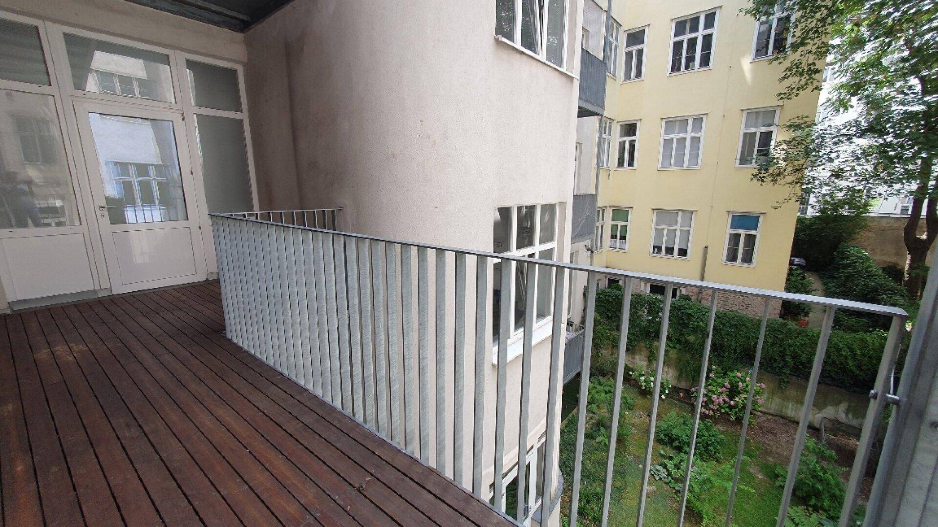Balkon mit Holzboden und Metallgeländer, bietet einen Blick auf den Innenhof.