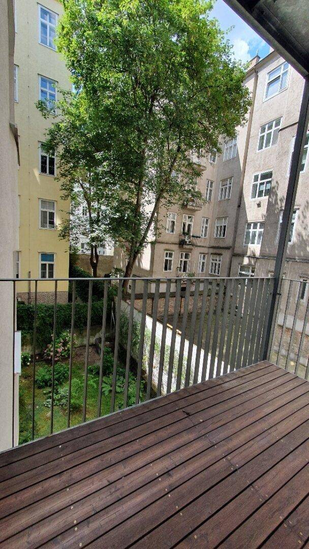 Geräumiger Balkon mit Holzdielen und Blick auf den begrünten Innenhof mit Bäumen.