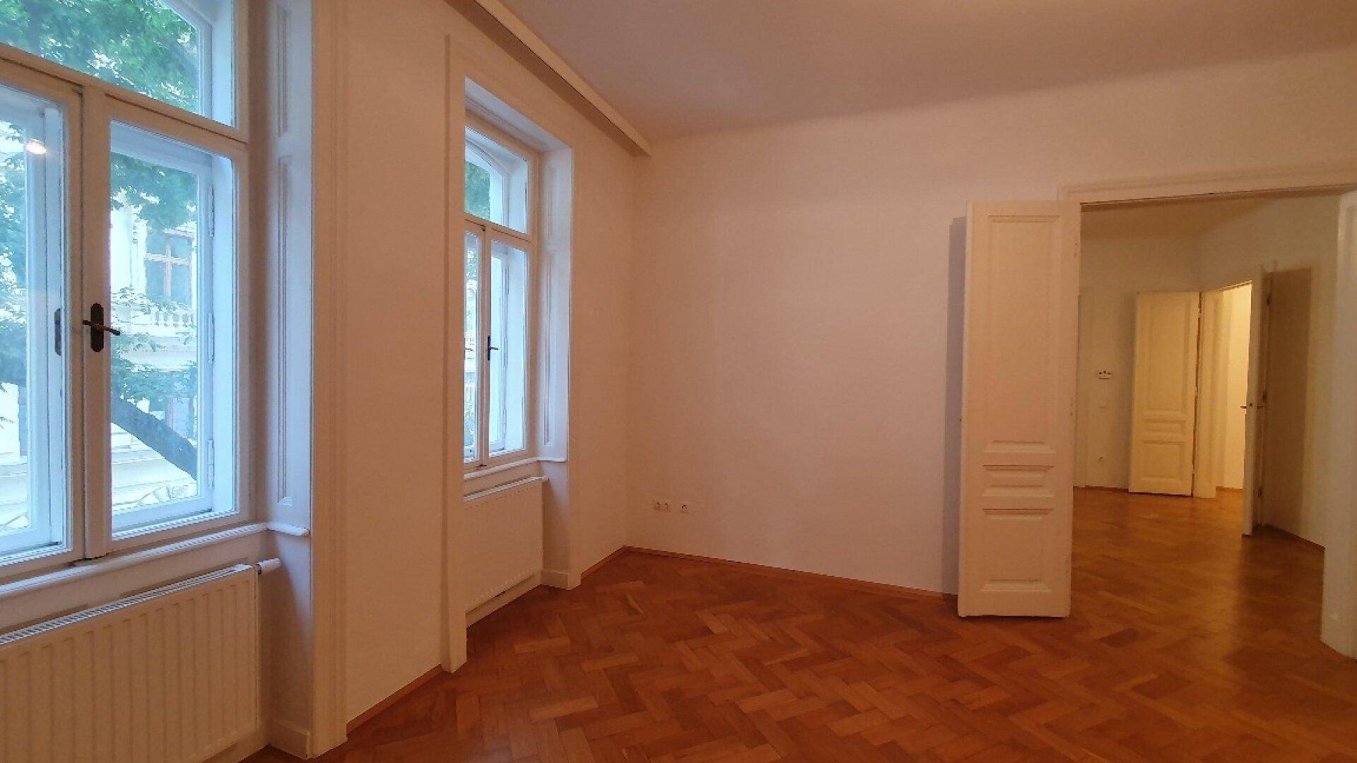 Geräumiges Zimmer mit klassischem Fischgrätparkett und Blick ins Grüne durch die Fenster.