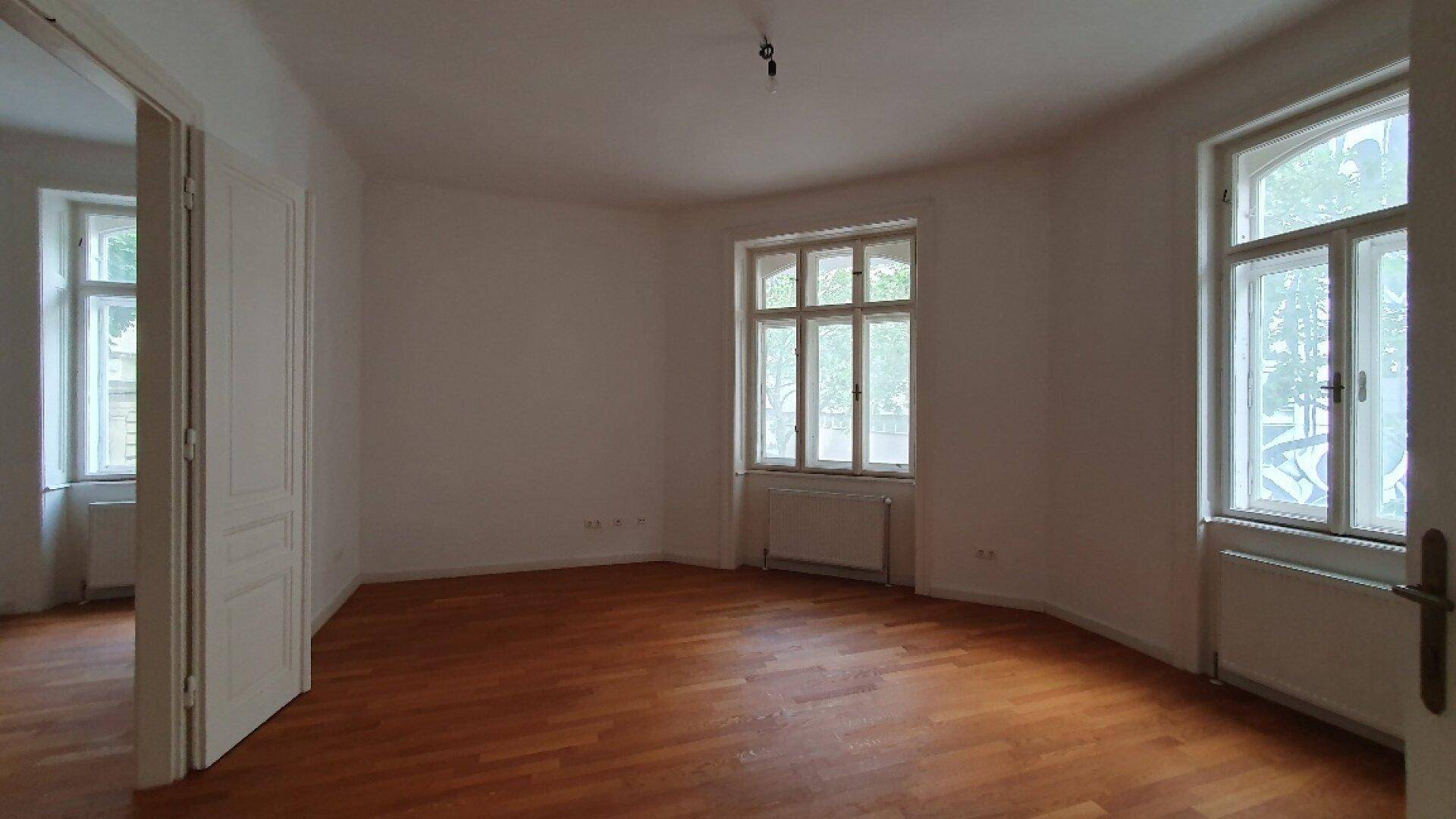 Großzügiger Raum mit Holzboden und hohen Fenstern, ideal für Wohn- oder Schlafbereich.