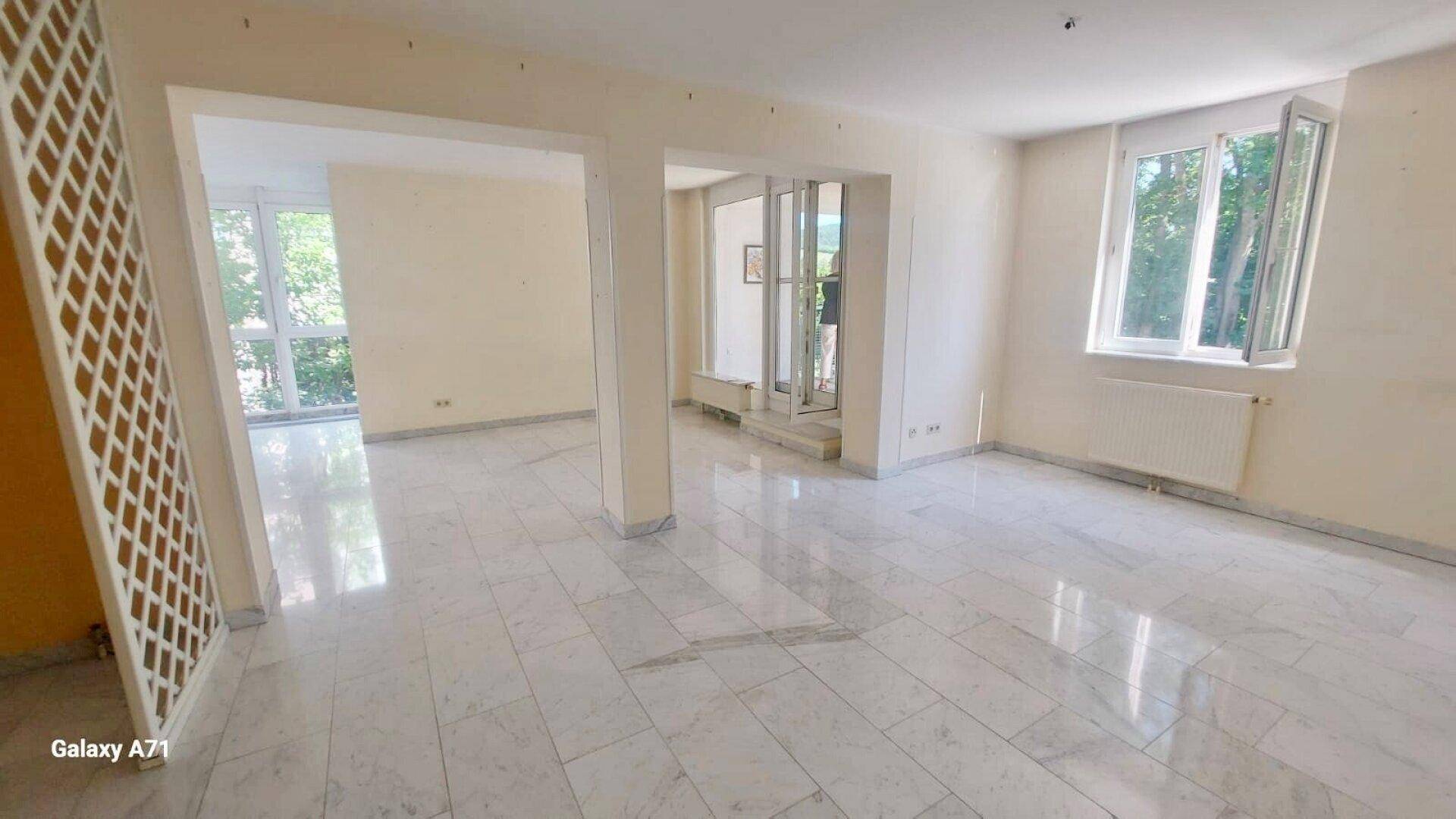 Geräumiges Wohnzimmer mit hellem Marmorboden und großen Fensterfronten für viel Tageslicht.