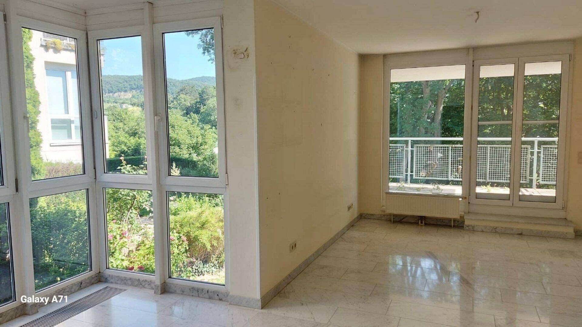 Helles Wohnzimmer mit großen Fenstern, die einen Blick ins Grüne bieten, und Marmorboden.