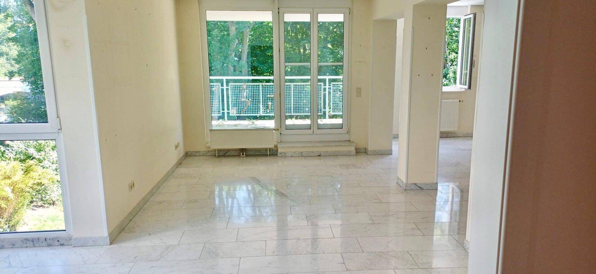 Heller Wohnbereich mit Marmorboden und Zugang zu einem Balkon mit Blick ins Grüne.