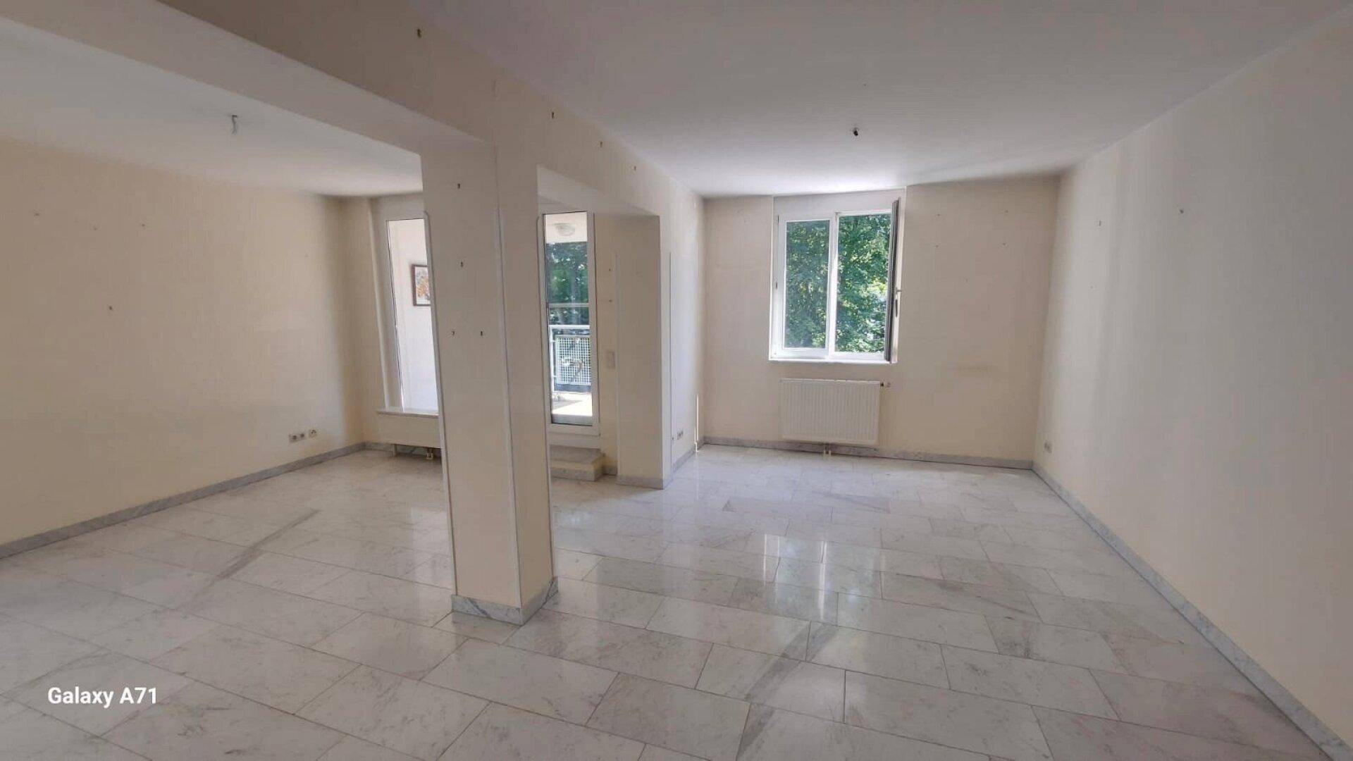 Großzügiges Wohnzimmer mit Marmorboden und Fenstern, die viel natürliches Licht hereinlassen.