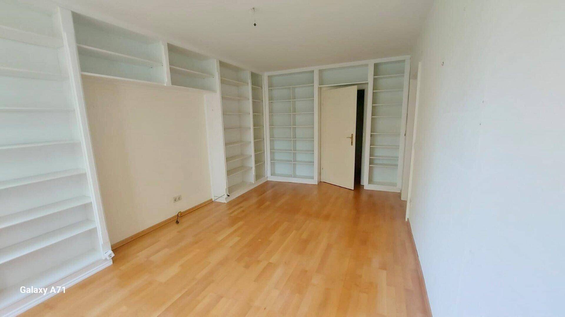 Geräumiges Zimmer mit Holzparkett und weißen Einbauregalen, die viel Stauraum bieten.