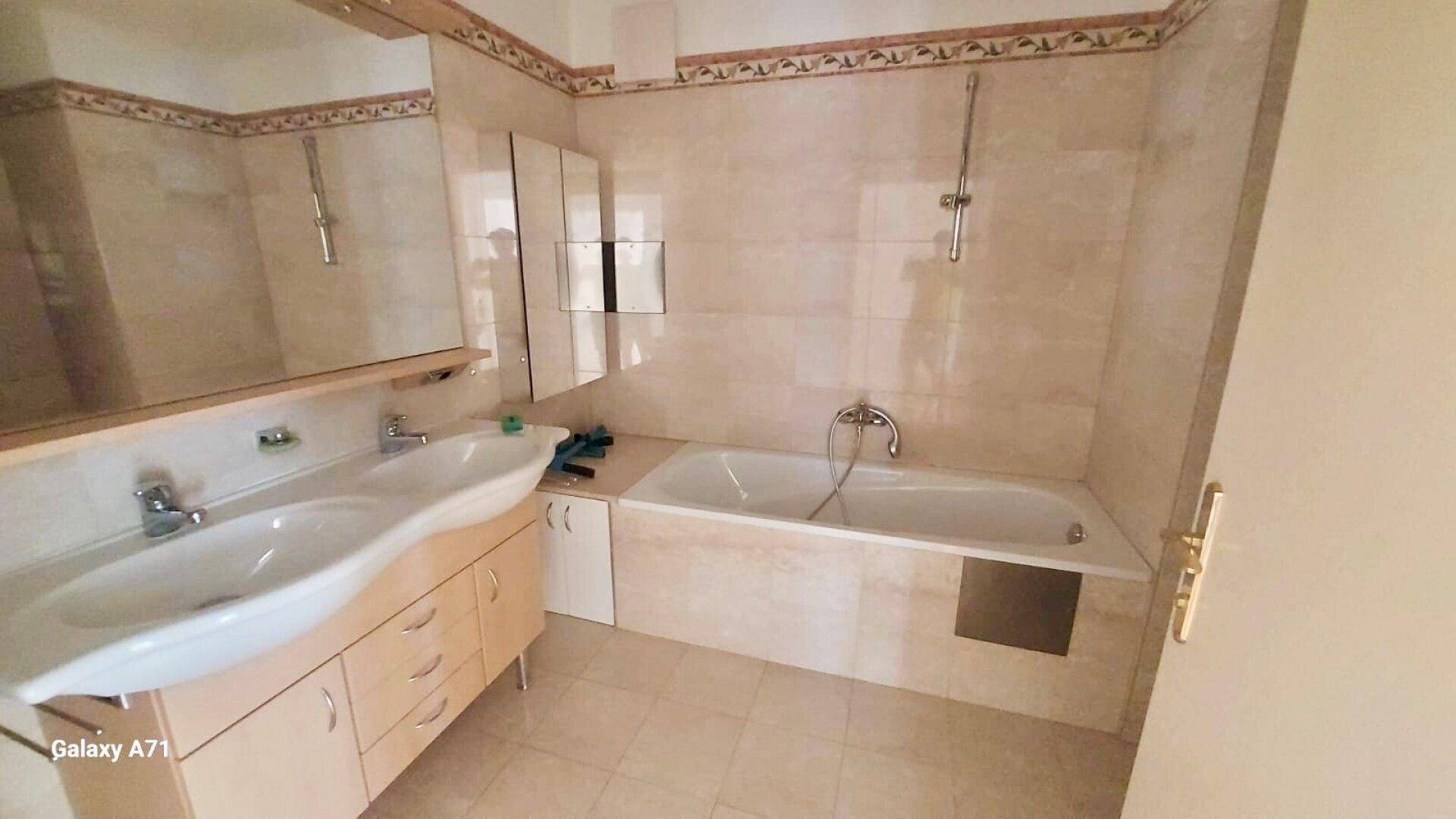 Badezimmer mit Doppelwaschbecken, Badewanne und beigefarbenen Fliesen.