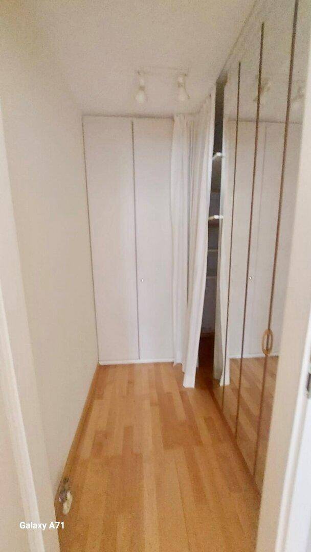 Begehbarer Kleiderschrank mit Spiegeltüren und hellem Holzparkettboden.