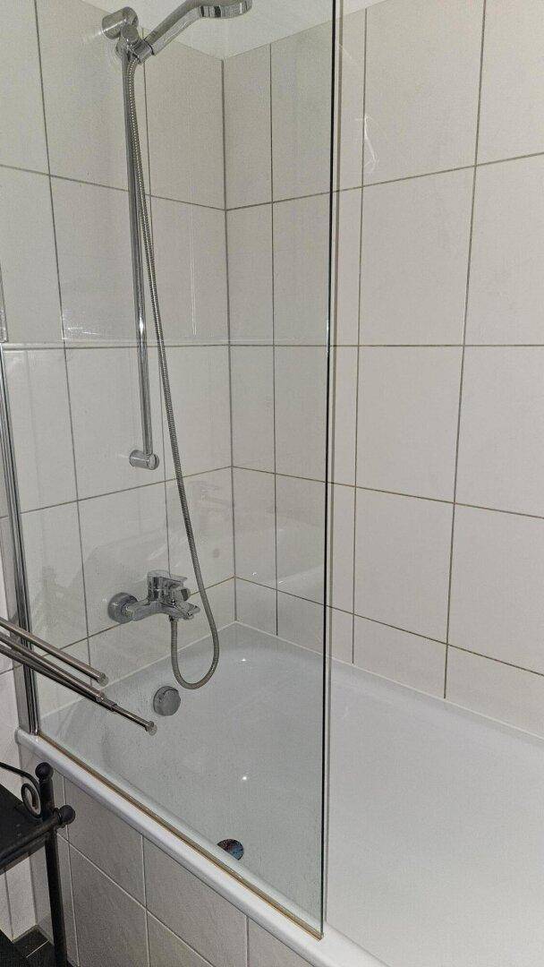 Badewanne mit Duschfunktion und Glasabtrennung in einem gefliesten Badezimmer.