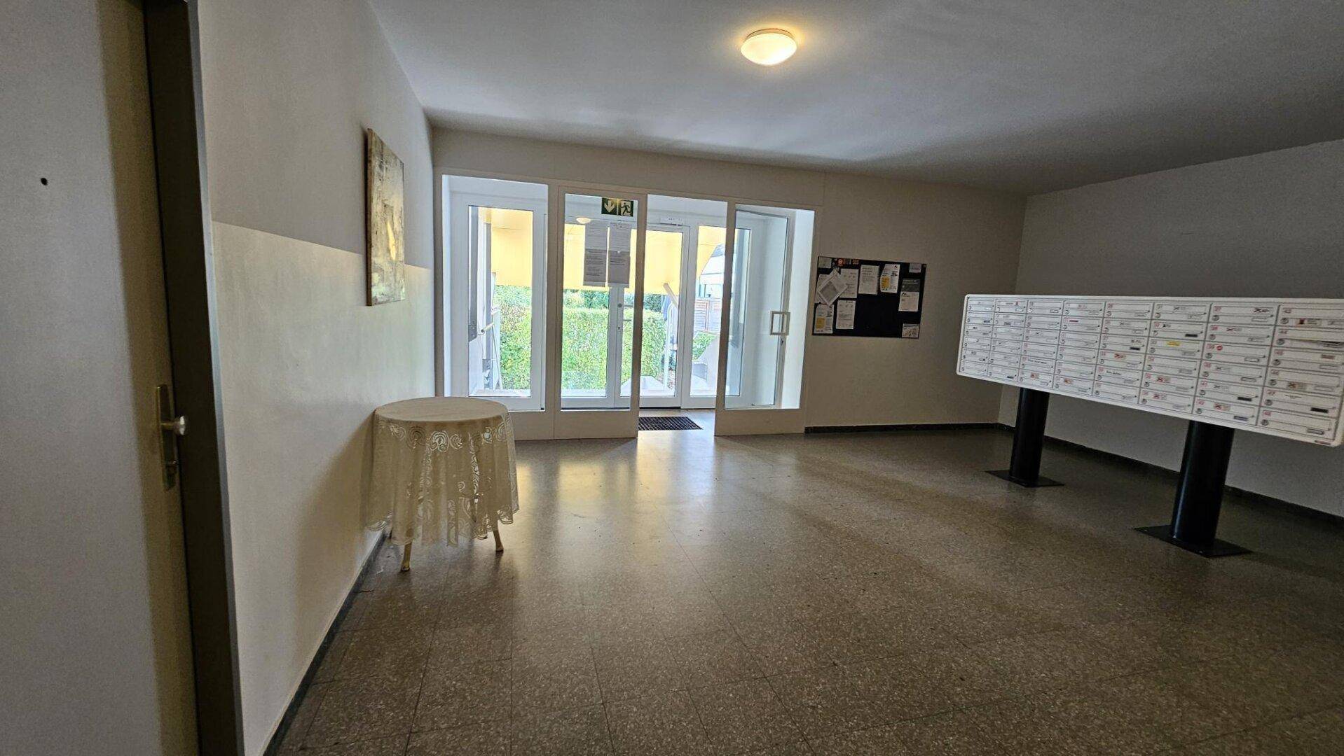 Heller Eingangsbereich des Gebäudes mit Briefkästen und Zugang zum Außenbereich.