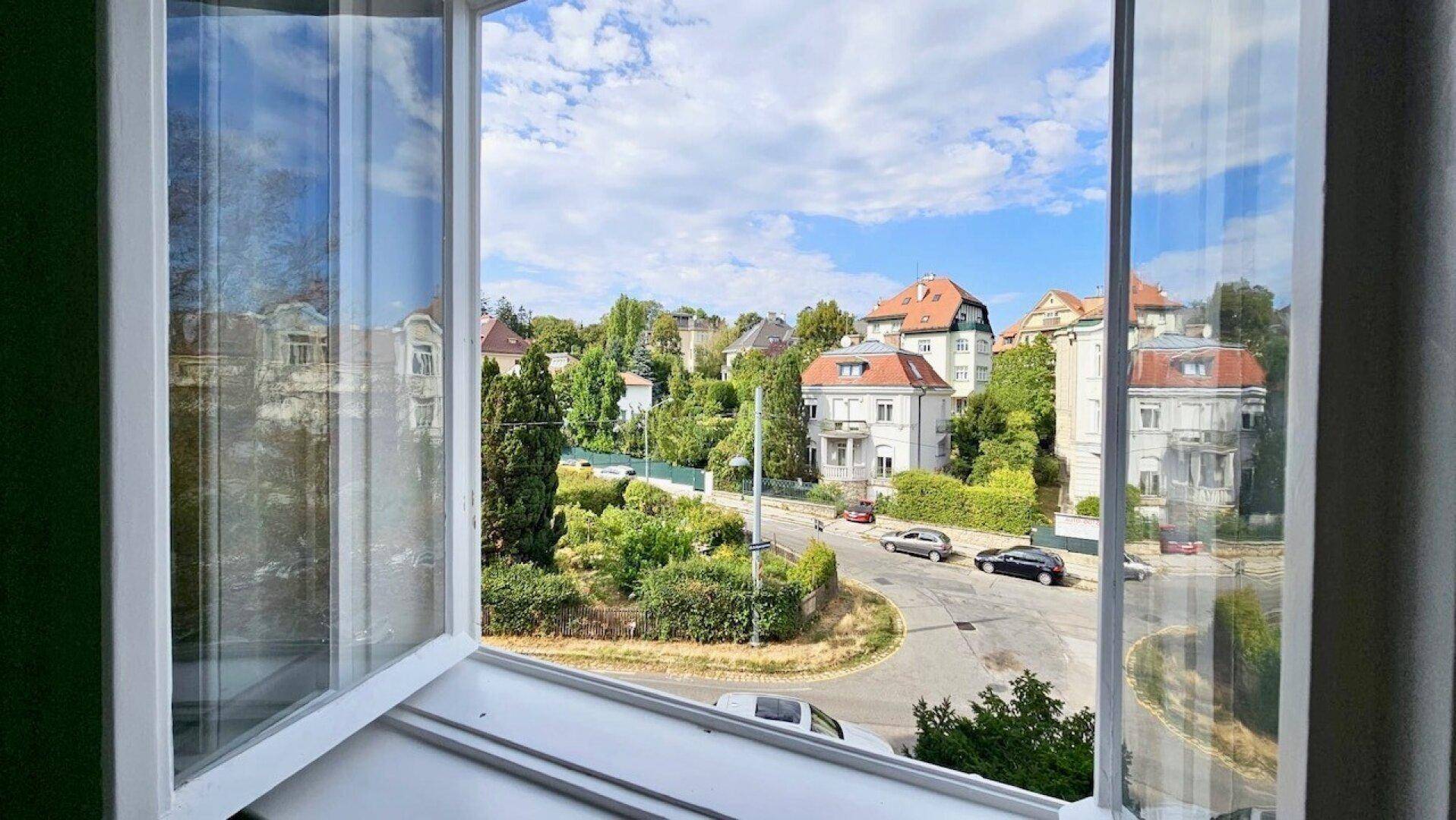 Panoramablick aus dem Fenster auf eine ruhige Wohnstraße mit charmanten Häusern und viel Grün.
