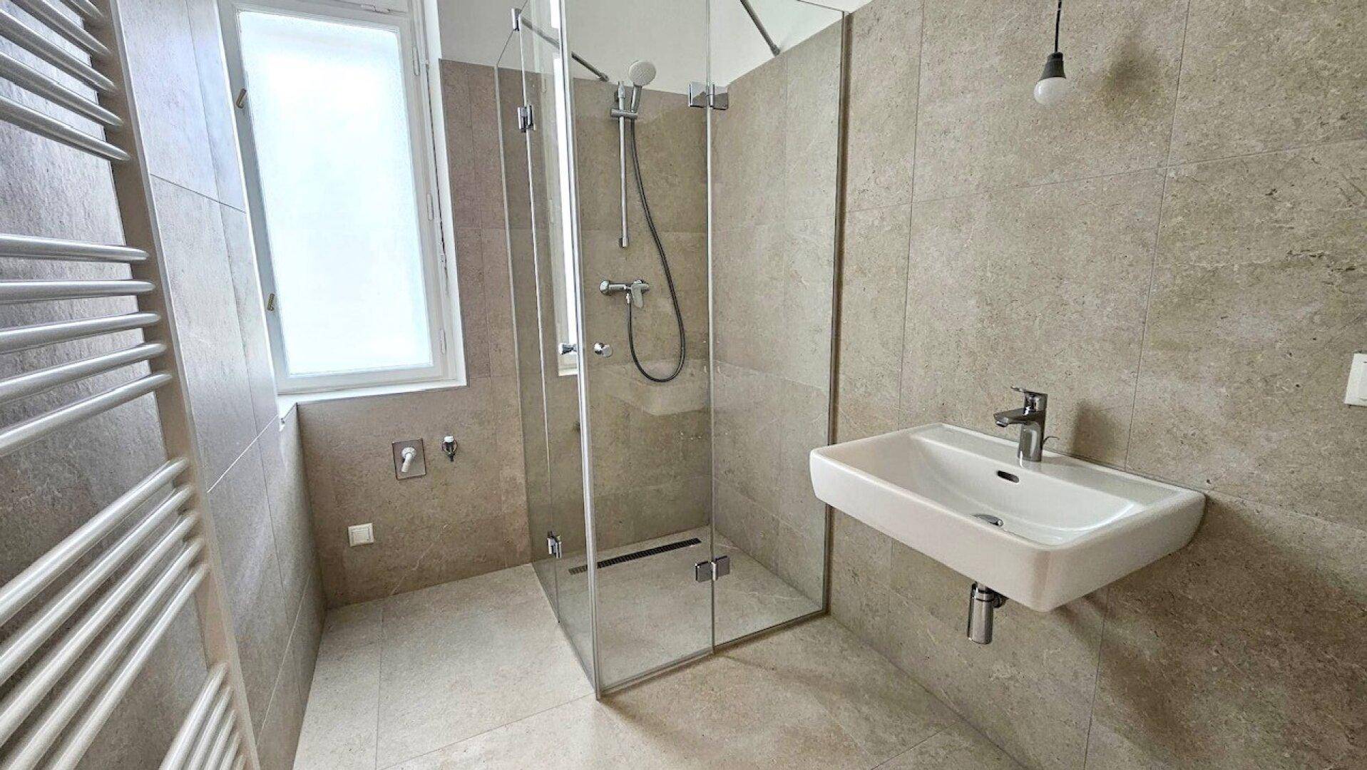 Modernes Badezimmer mit grauen Fliesen, begehbarer Dusche, Wandwaschbecken und Handtuchheizkörper.