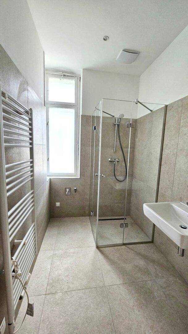 Helles Badezimmer mit modernen grauen Fliesen, einer geräumigen begehbaren Dusche und Fenster.