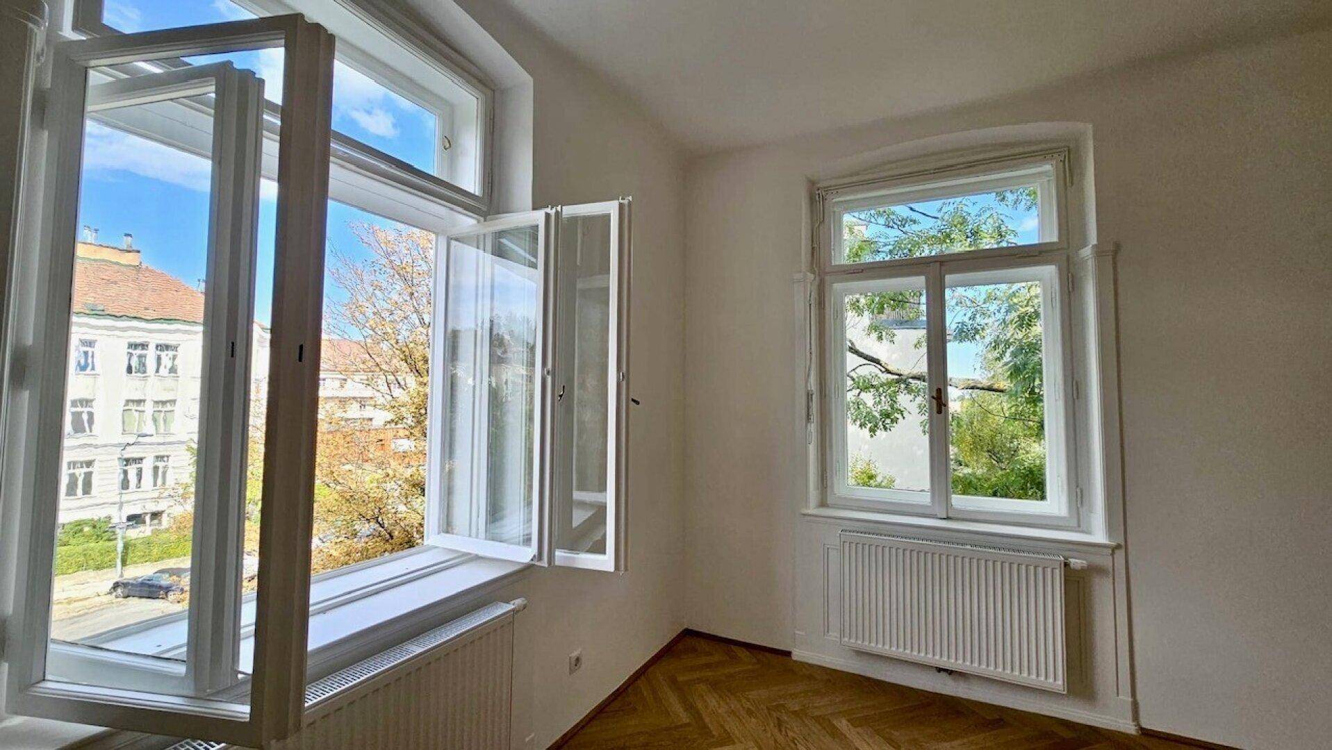 Geöffnete Fenster bieten einen weiten Blick auf die Umgebung mit Gebäuden und Bäumen.