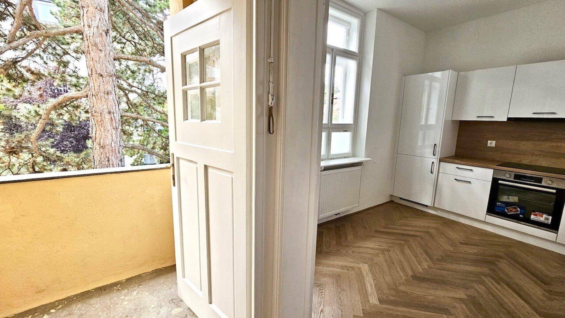 Küche mit Zugang zu einem kleinen Balkon oder einer Loggia, umgeben von grünen Bäumen.