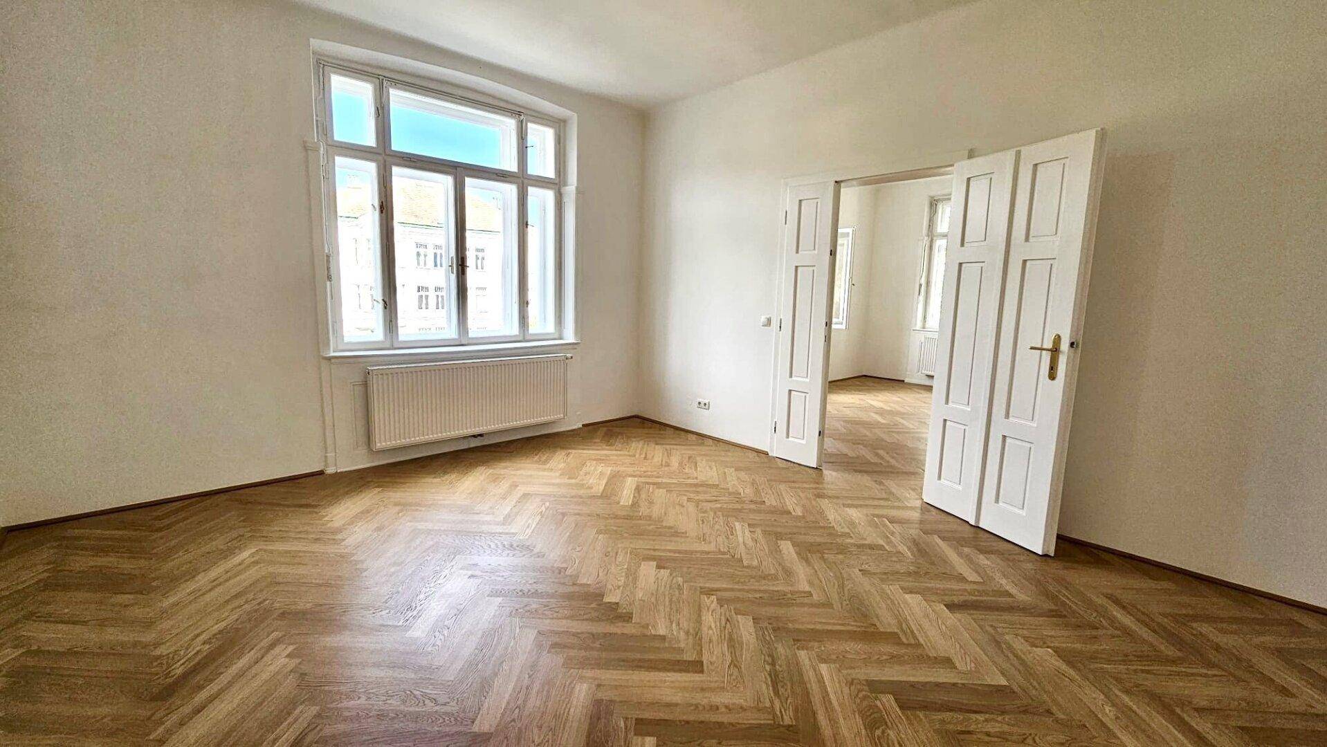 Helles Wohnzimmer mit elegantem Fischgrätparkett und Doppeltüren zu einem weiteren Raum.