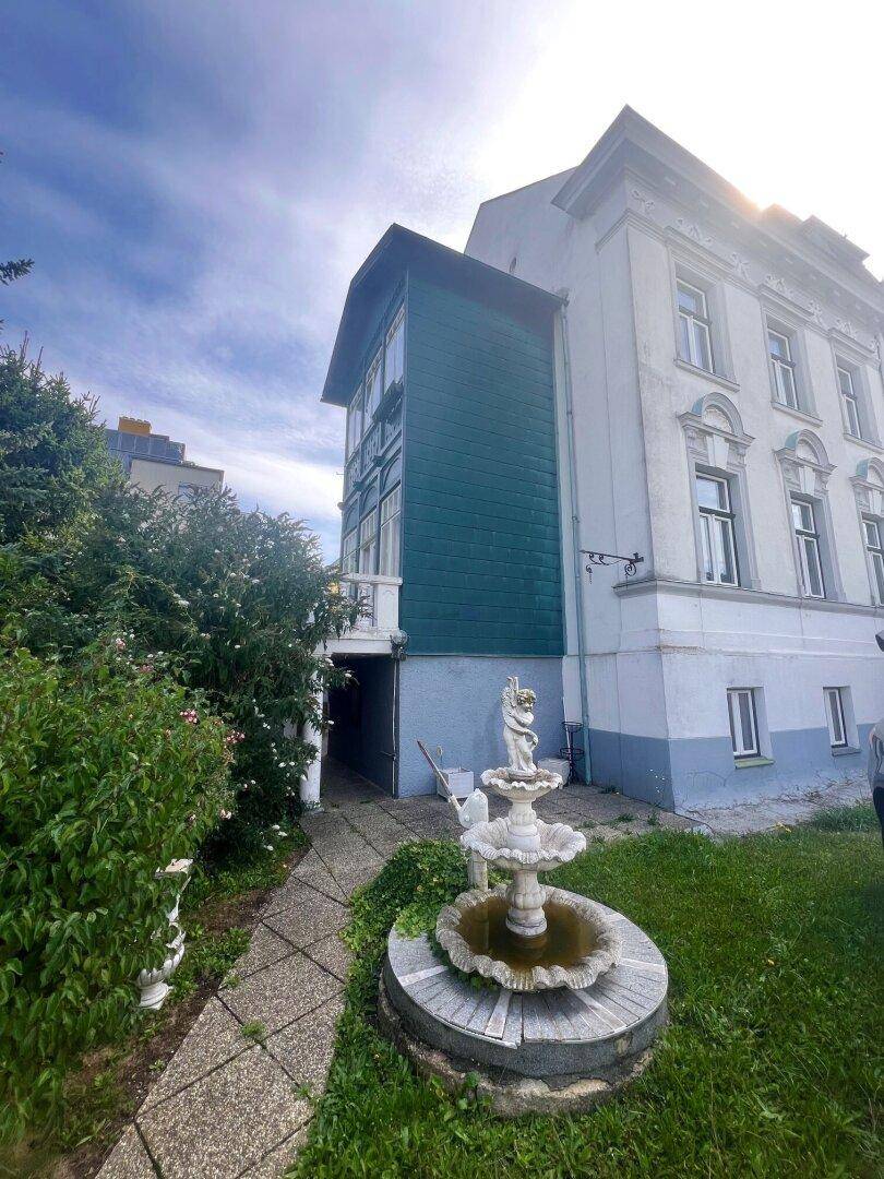 Seitenansicht des Gebäudes mit einem dekorativen Brunnen und einem gepflasterten Weg im Garten.