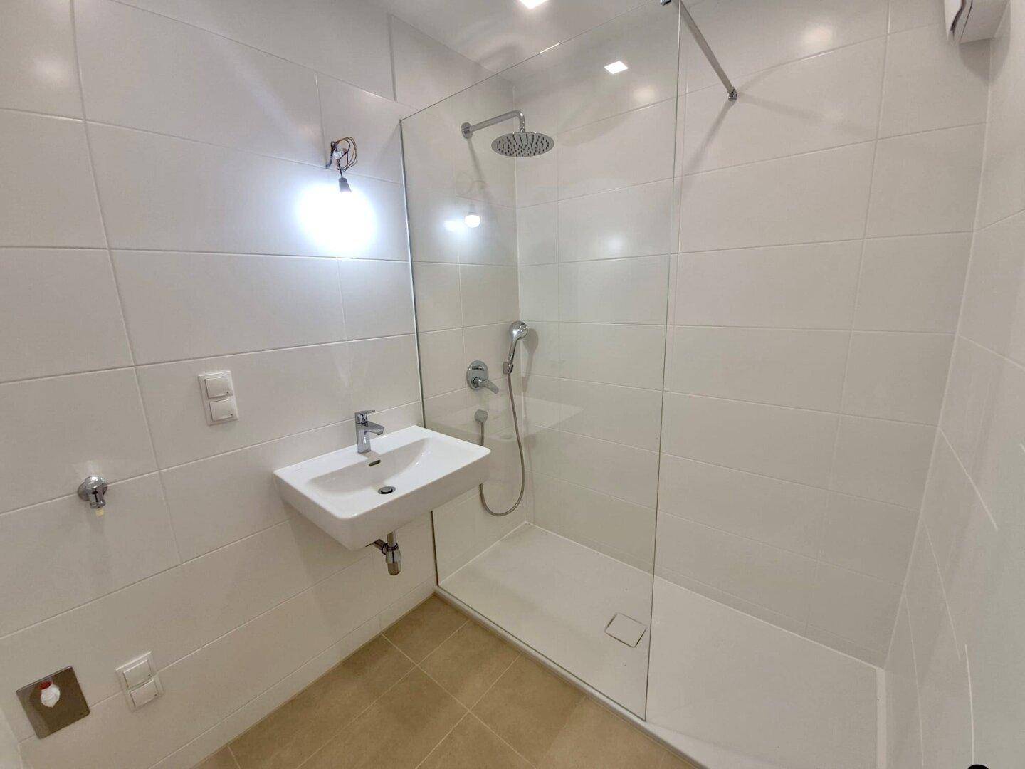 Modernes Badezimmer mit weißen Fliesen, einer ebenerdigen Dusche und einem einzelnen Waschbecken.