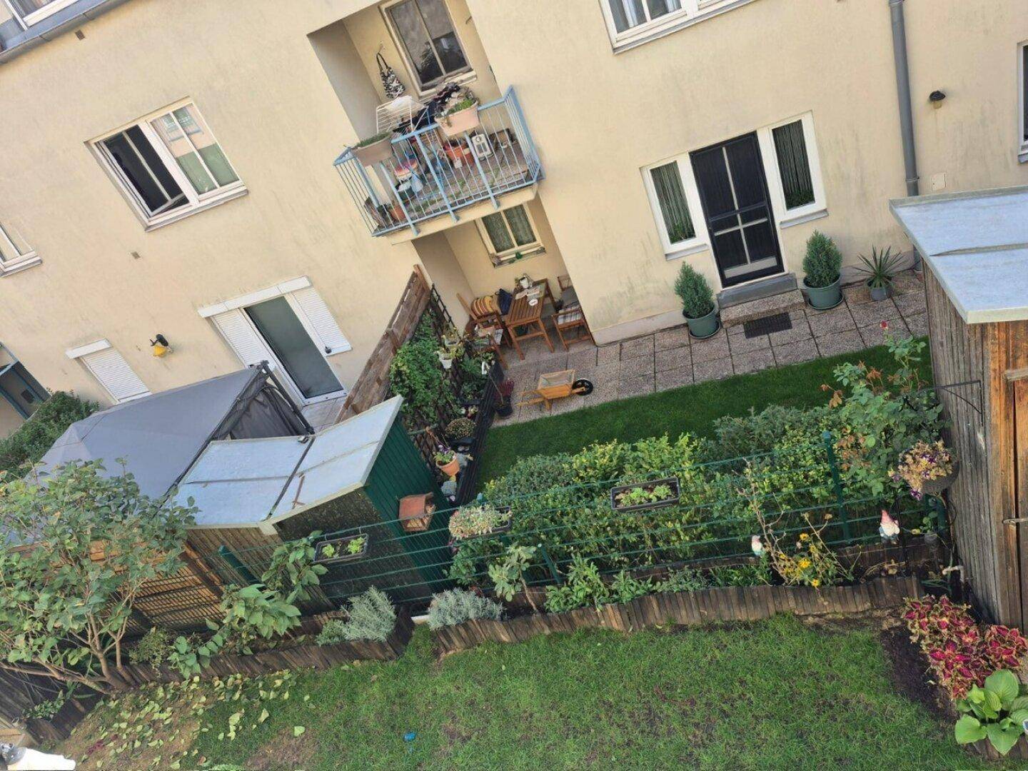 Blick von oben auf einen gepflegten Gartenbereich mit Rasen, Pflanzen und kleinen Schuppen.