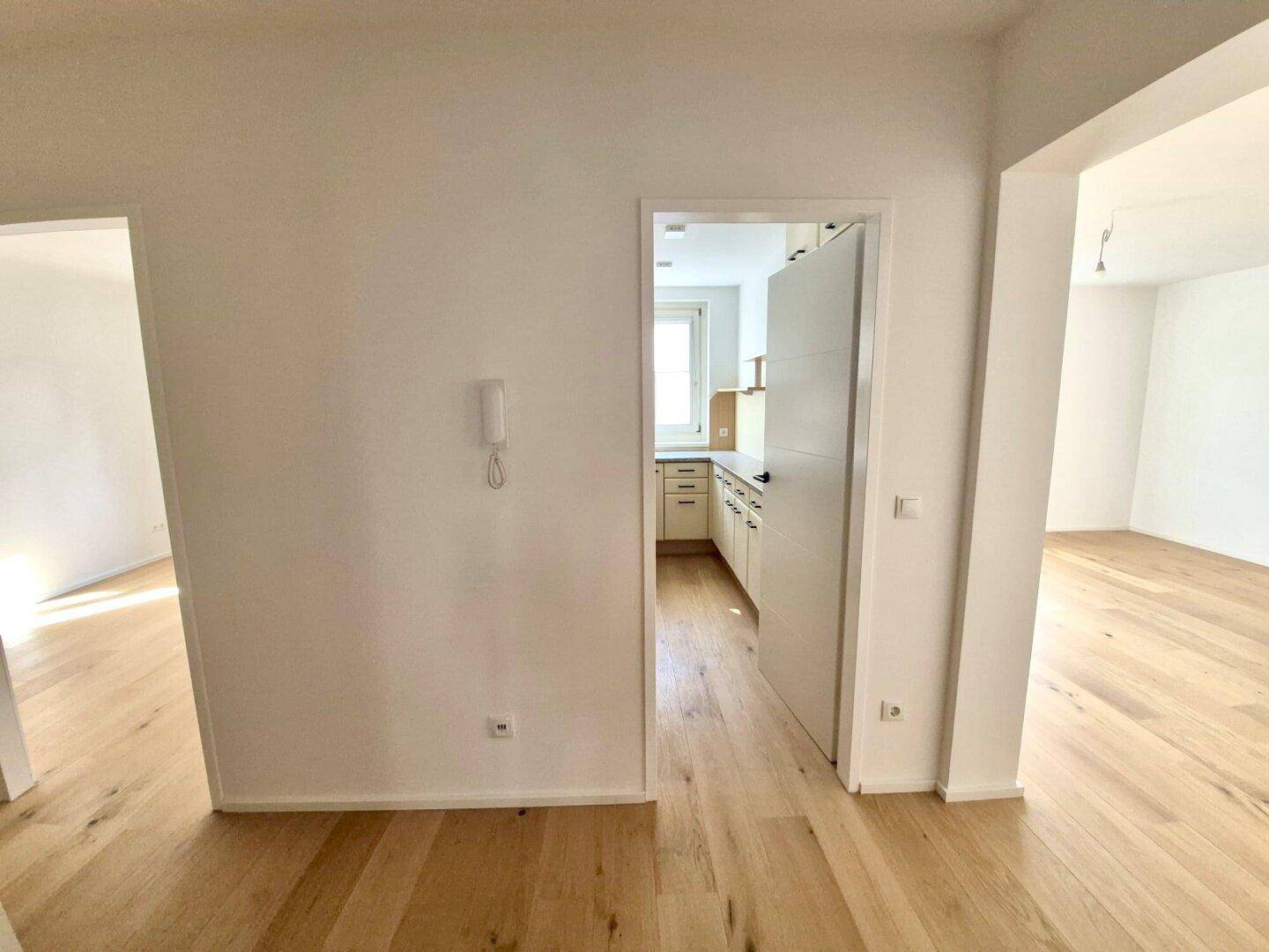Heller Flur mit Holzboden, der den Blick in die Küche und einen weiteren Raum freigibt.