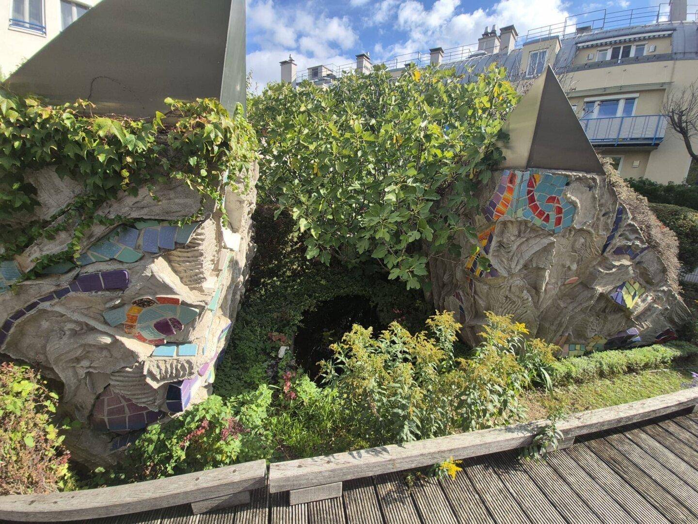 Künstlerisch gestalteter Gartenbereich mit Mosaik-Skulpturen und üppiger Vegetation.