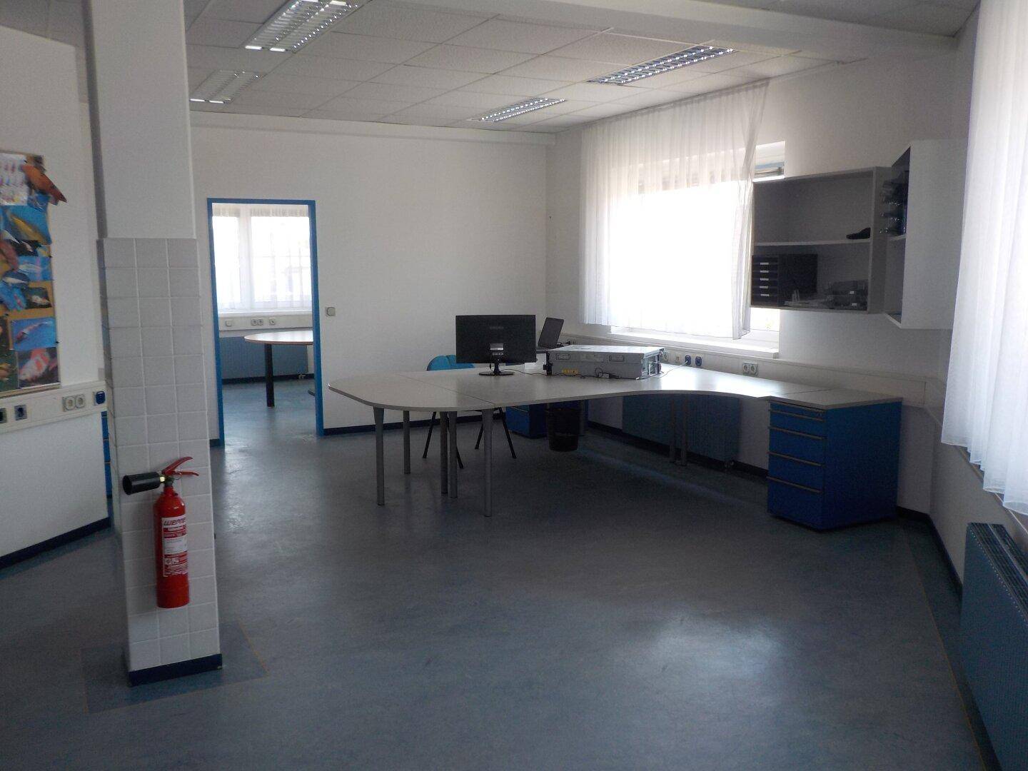 Großes Büro mit mehreren Arbeitsplätzen, Computern und einem Feuerlöscher an der Säule.