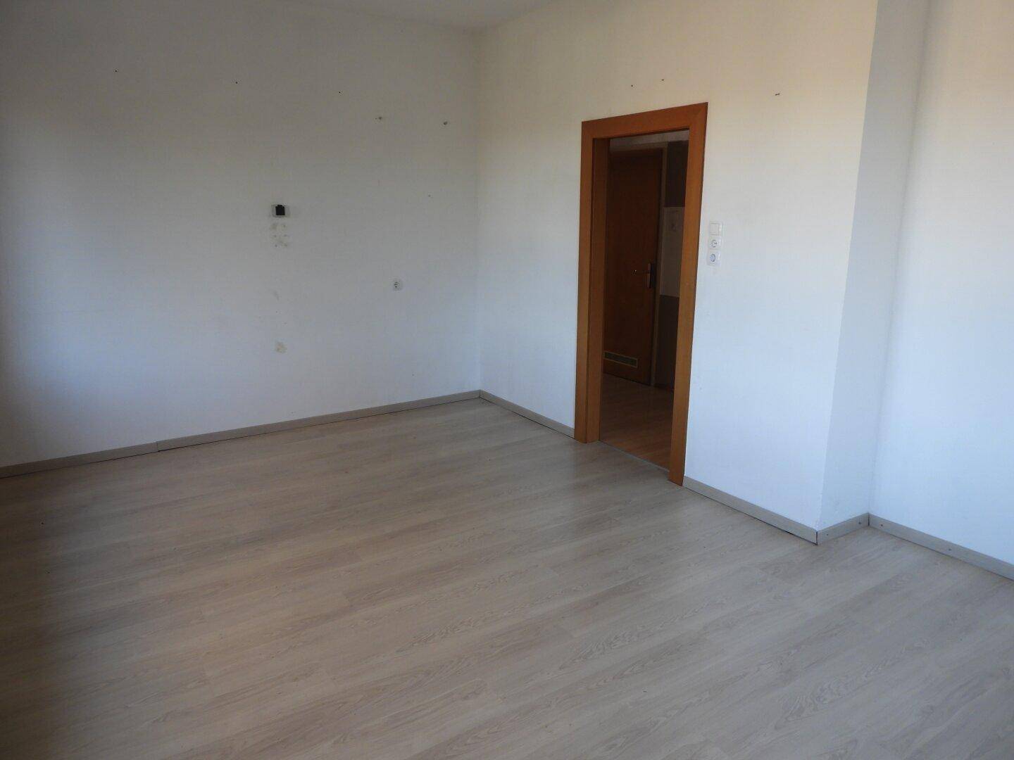 Leeres Zimmer mit hellem Laminatboden und Holztür, bereit für neue Bewohner und Gestaltung.