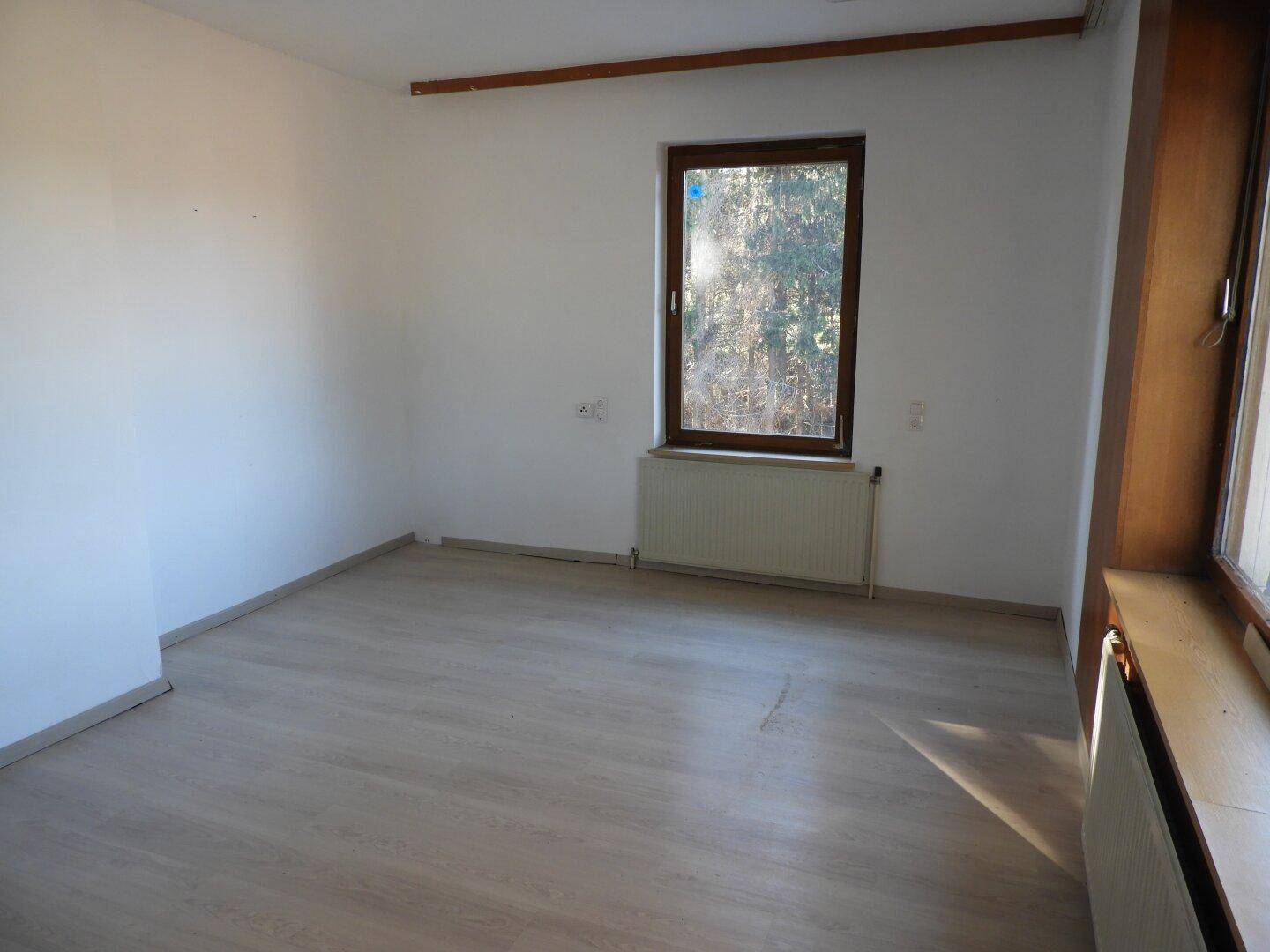 Geräumiges Zimmer mit Laminatboden und großem Fenster, das viel Tageslicht hereinlässt.