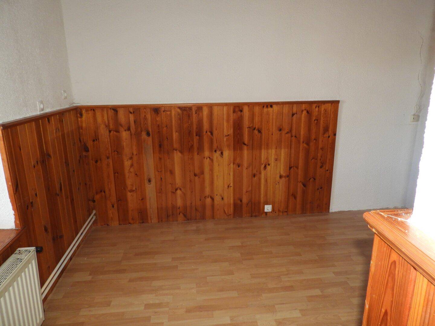 Zimmer mit Holzvertäfelung an den Wänden und hellem Laminatboden, bereit zur individuellen Gestaltung.
