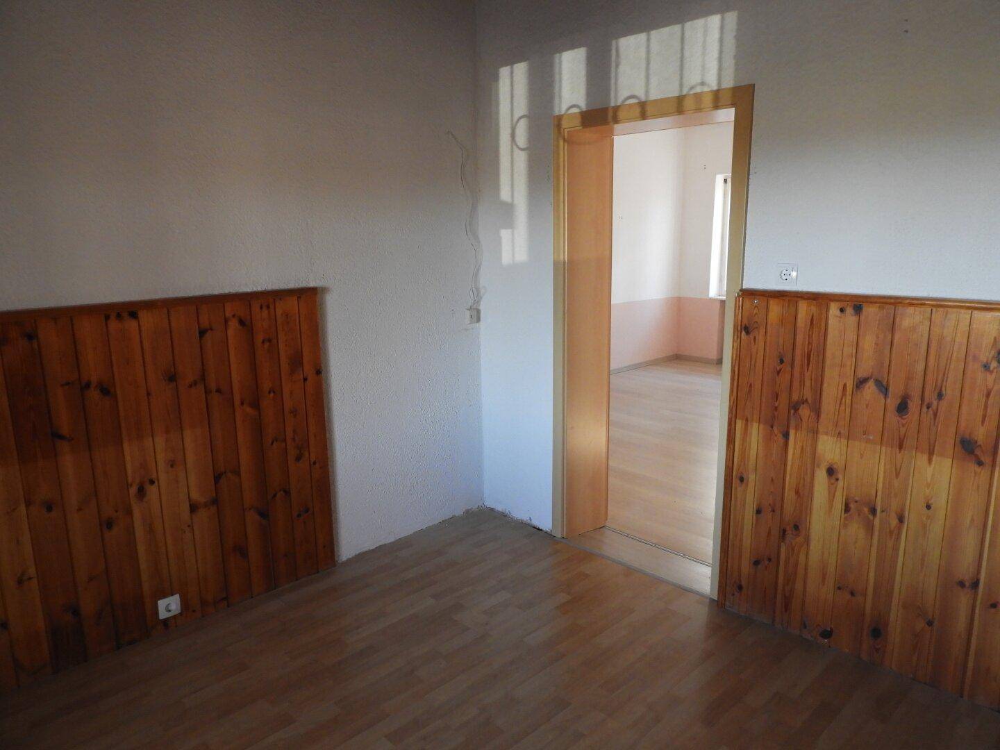 Zimmer mit Holzvertäfelung und Laminatboden, mit Blick in einen angrenzenden Raum.