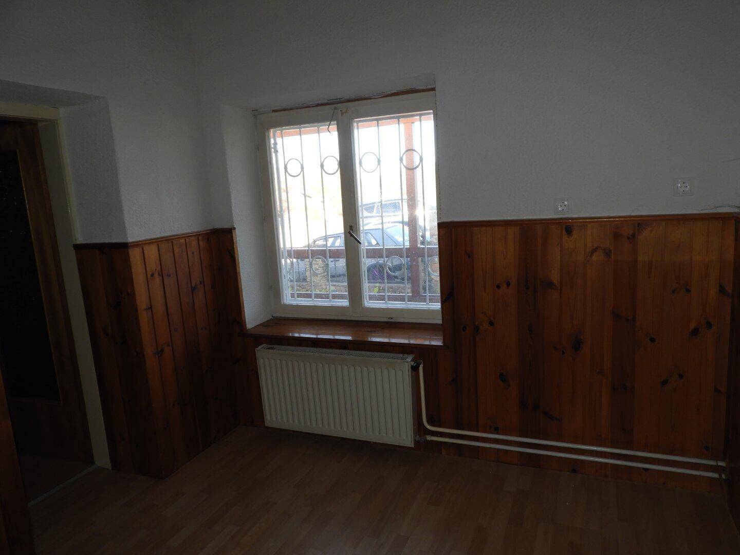 Zimmer mit Holzvertäfelung und Fenster mit Gitter, das Tageslicht hereinlässt.