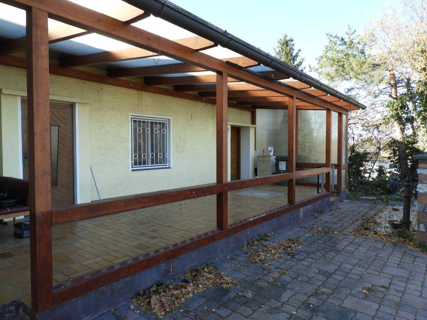 Überdachte Terrasse mit Holzbalkenkonstruktion und gefliestem Boden, bereit zur Nutzung im Freien.