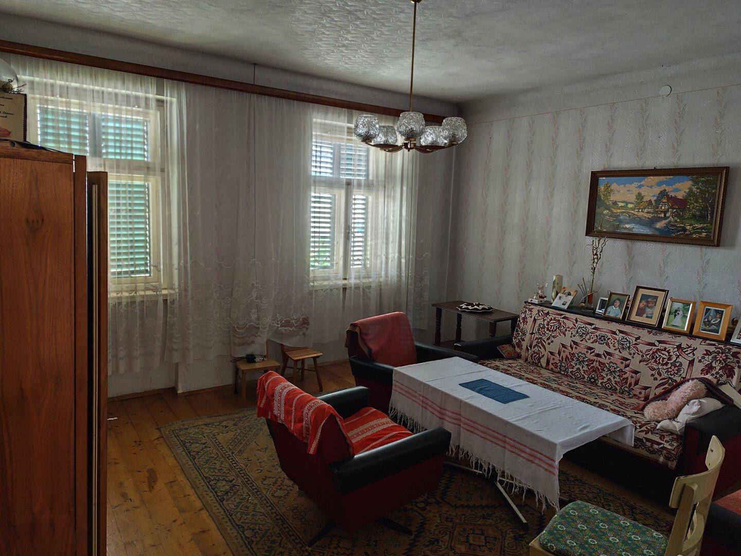 Gemütliches Wohnzimmer mit Holzboden, traditionellen Möbeln und gemusterter Tapete.