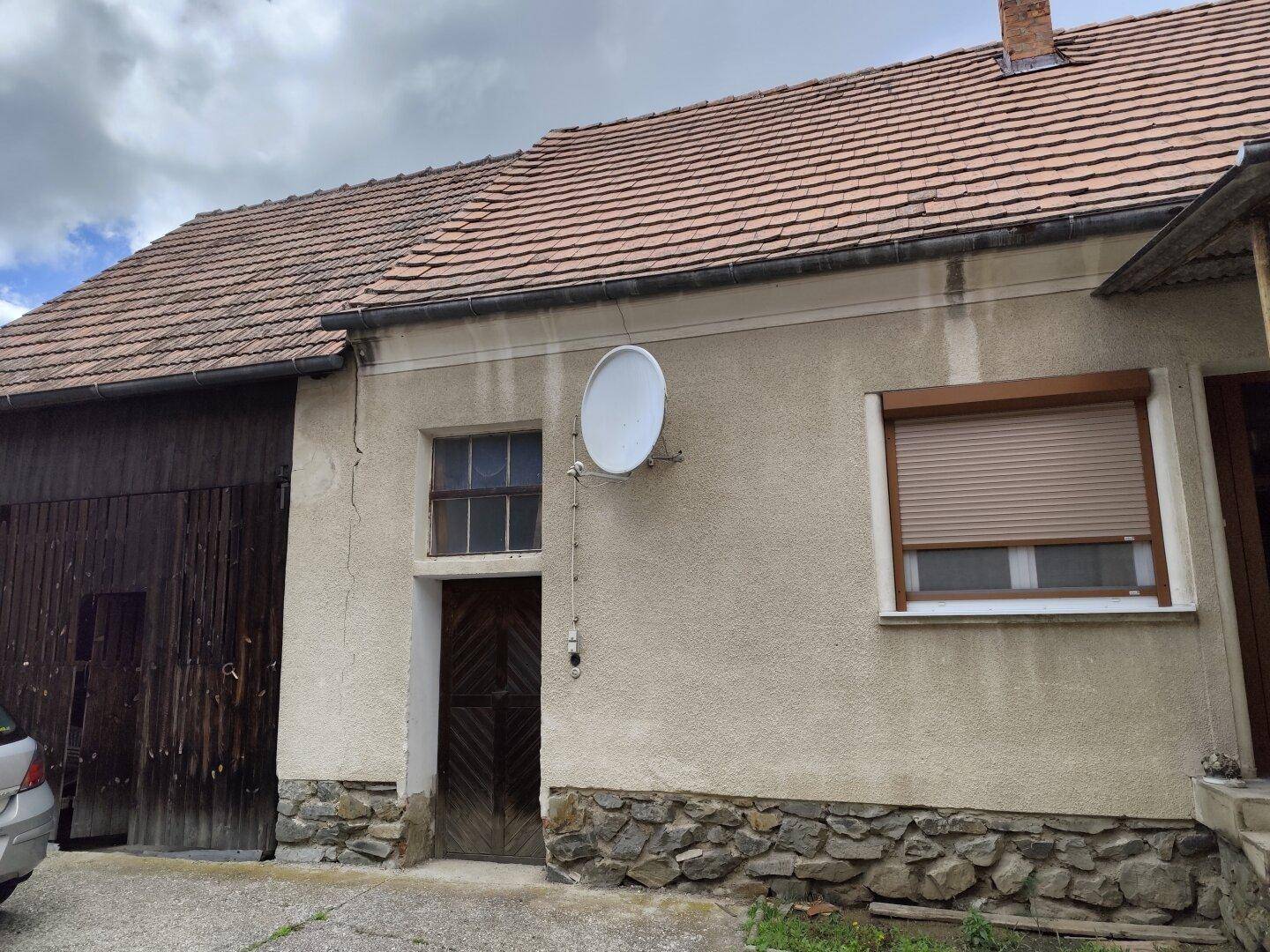 Seitenansicht eines Hauses mit Holztor, Putzfassade und Satellitenschüssel an der Wand.