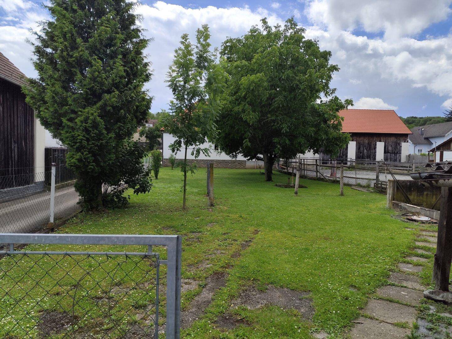Großer, grüner Garten mit Rasenfläche und mehreren Bäumen unter bewölktem Himmel.