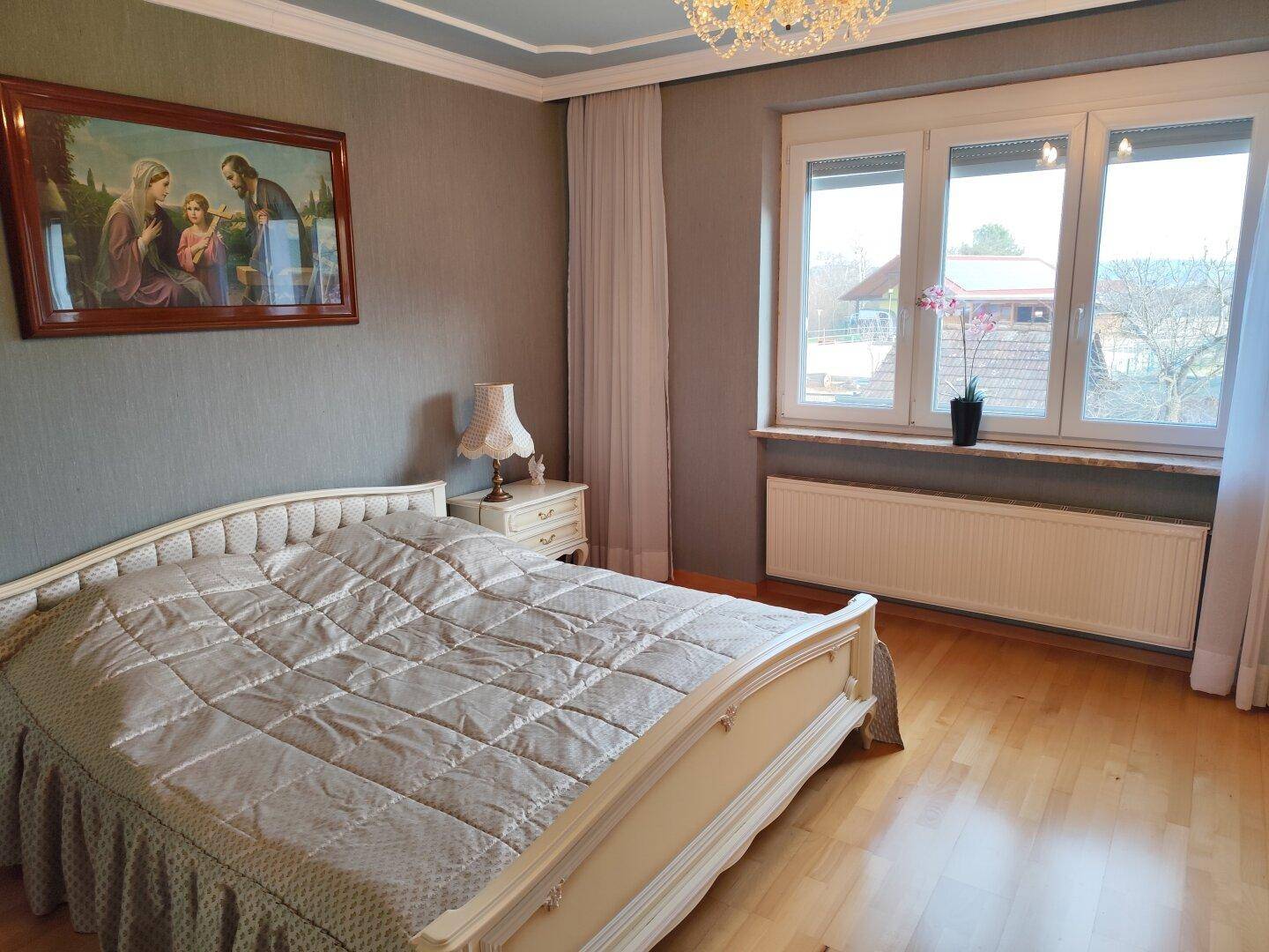 Helles Schlafzimmer mit klassischem Doppelbett, Parkettboden und Blick ins Grüne.