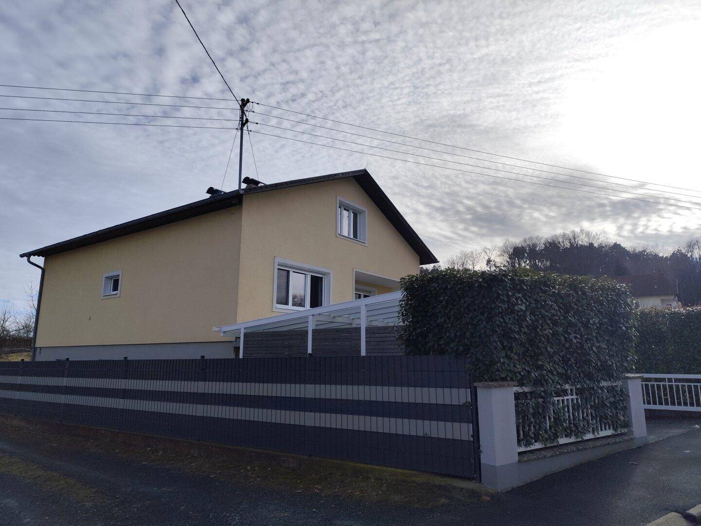 Seitenansicht des Hauses mit überdachtem Bereich und hohem Zaun.