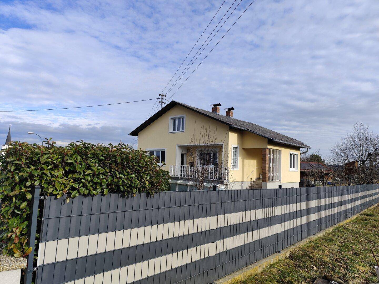 Ansicht des Hauses von der Seite mit Zaun und Blick auf die ländliche Umgebung.