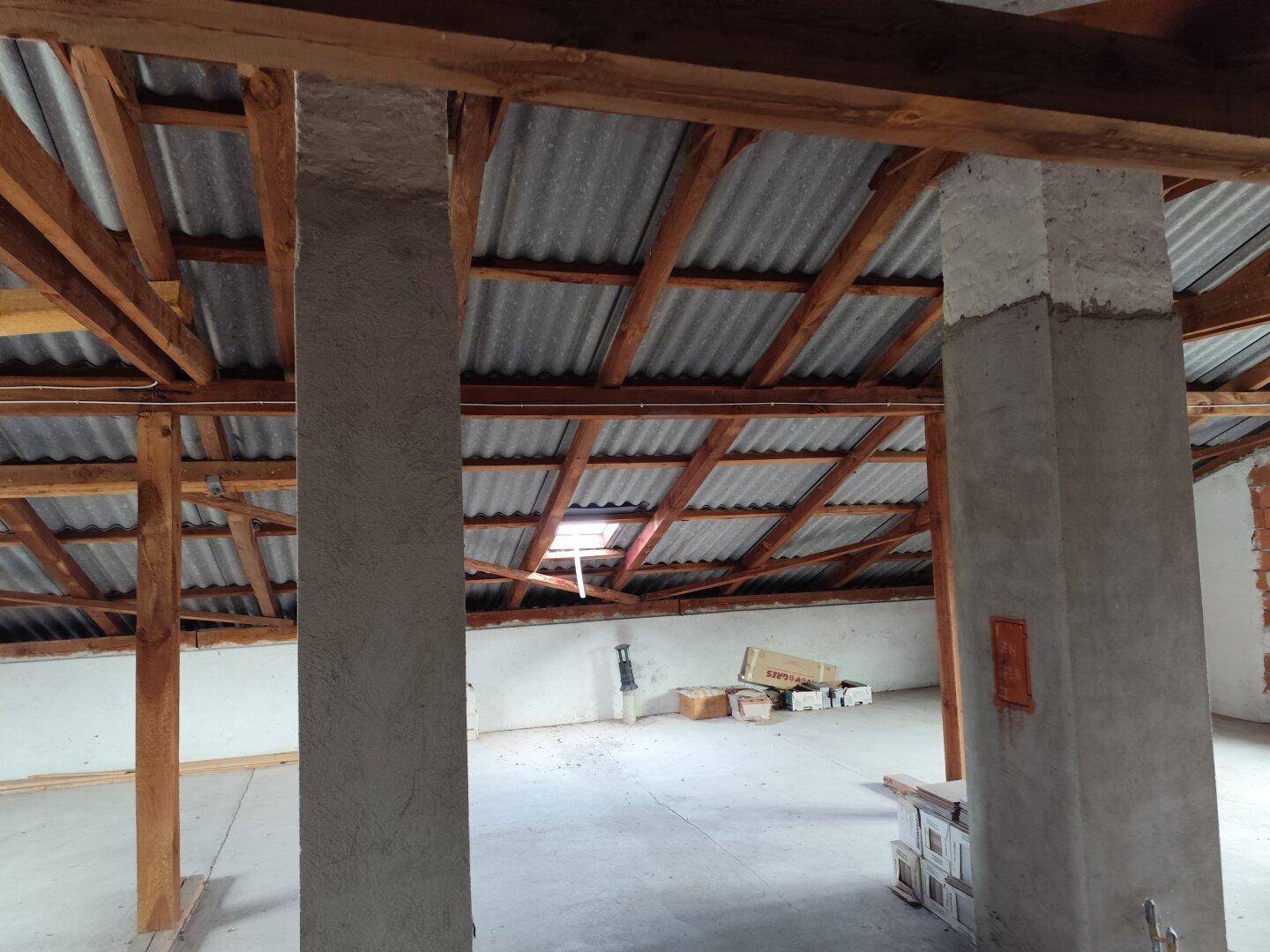 Geräumiger Dachboden mit Holzbalken und Betonboden, bereit für den Ausbau.