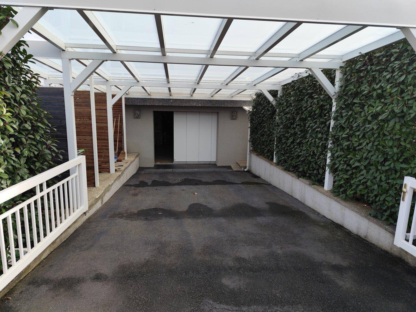 Überdachter Stellplatz vor der Garage, bietet Schutz für Fahrzeuge.