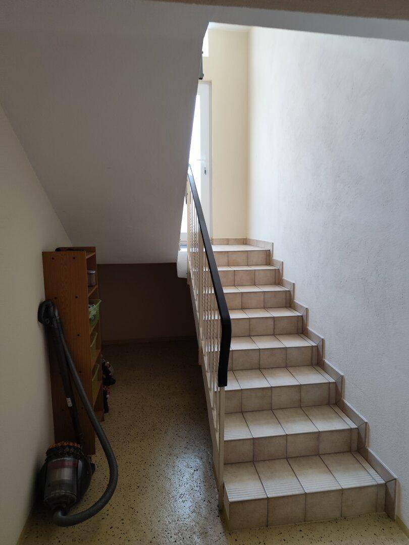 Treppenhaus mit gefliesten Stufen und Geländer, führt in die obere Etage.