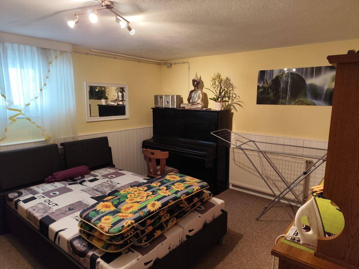 Vielseitiger Raum mit Bett, Klavier und Fenster, genutzt als Schlaf- oder Gästezimmer.