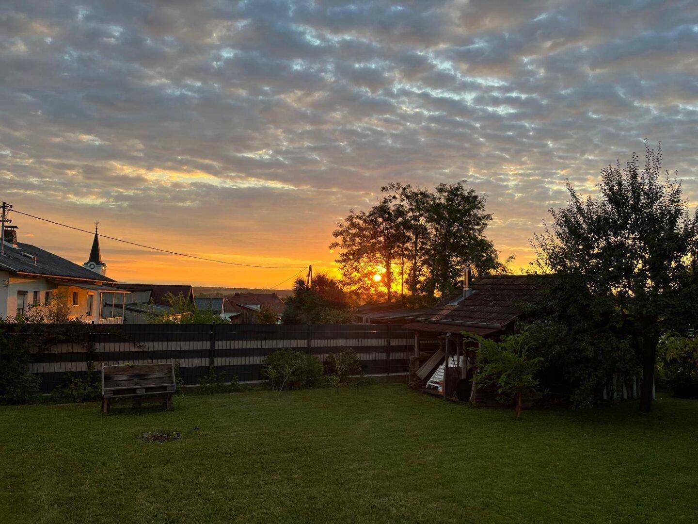 Großer Garten bei Sonnenuntergang mit Rasenfläche, Bäumen und Blick auf die Umgebung.